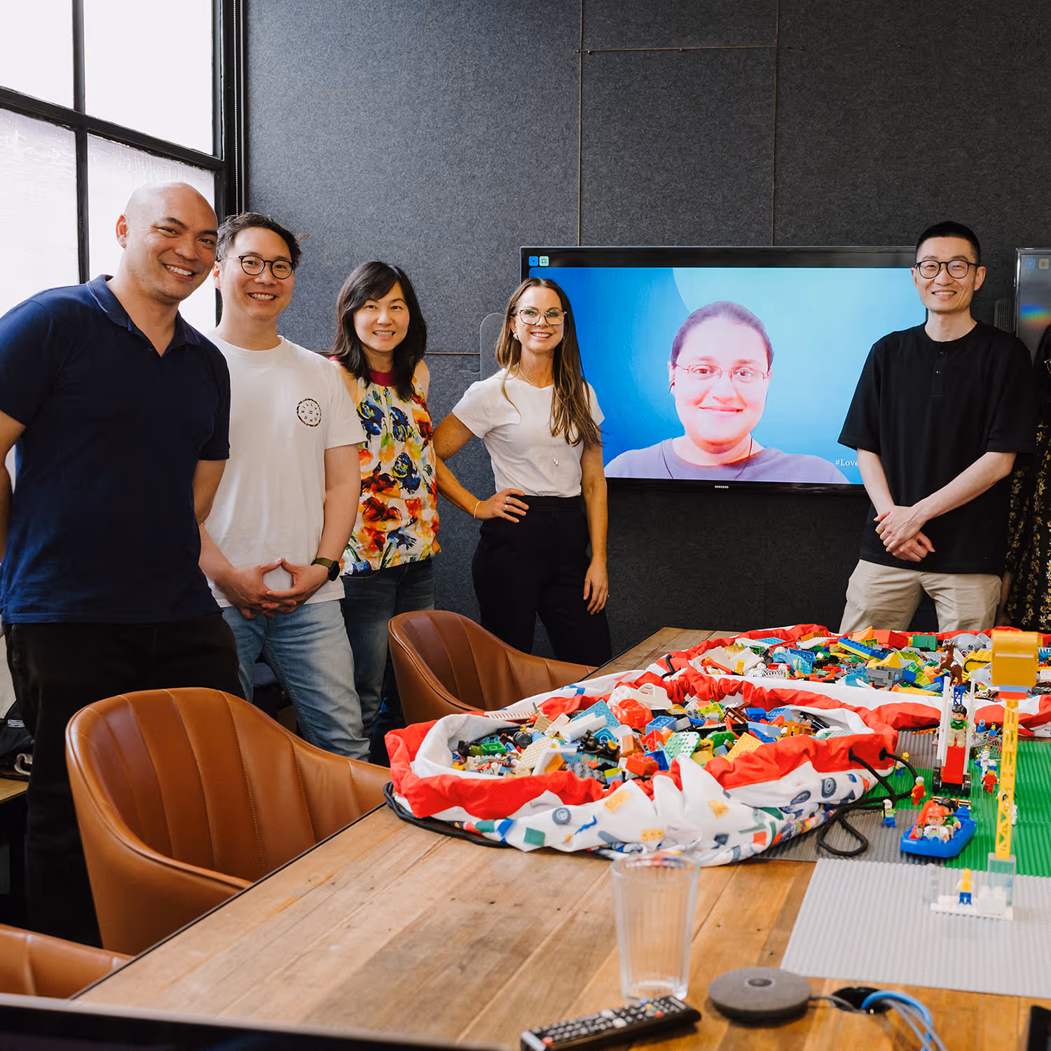 Colleagues gathered around a conference table as two women lean forward to shake hands, smiling and building rapport in a professional setting.
