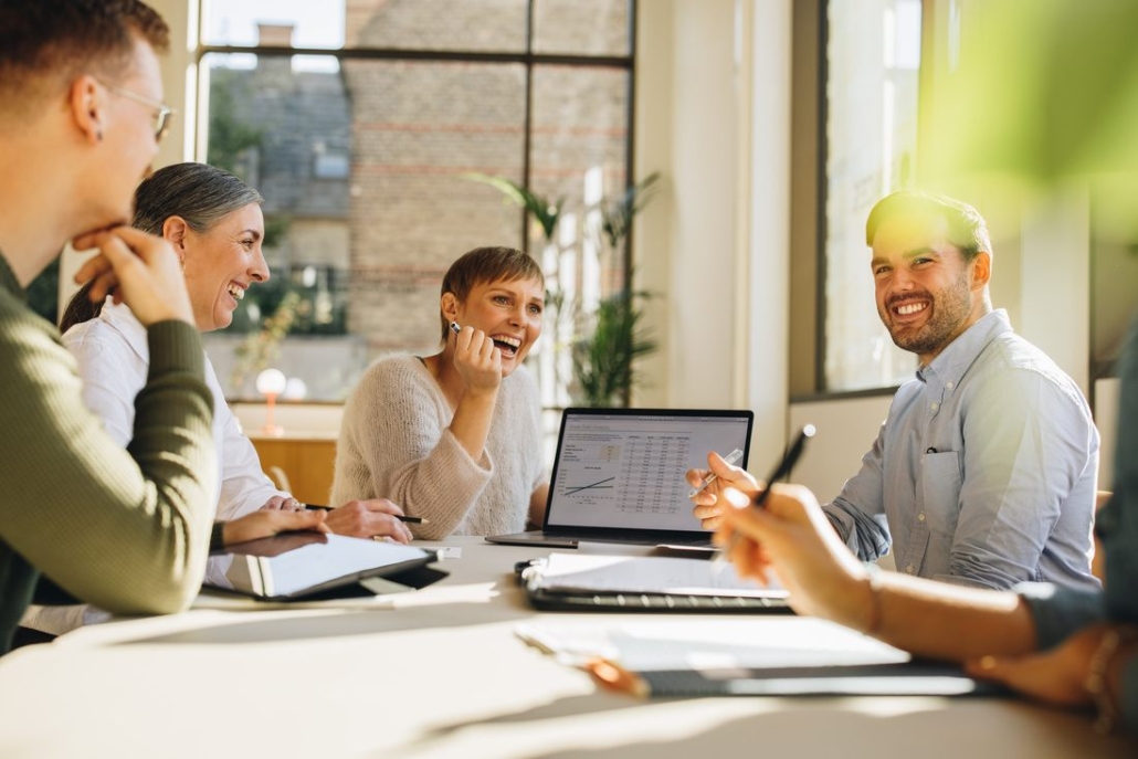 Four colleagues joining their fists together over a desk, symbolizing teamwork and unity during a collaborative meeting.