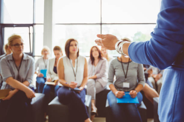 Facilitators standing at the front of a workshop while participants seated at tables applaud, creating an atmosphere of engagement and collaboration.