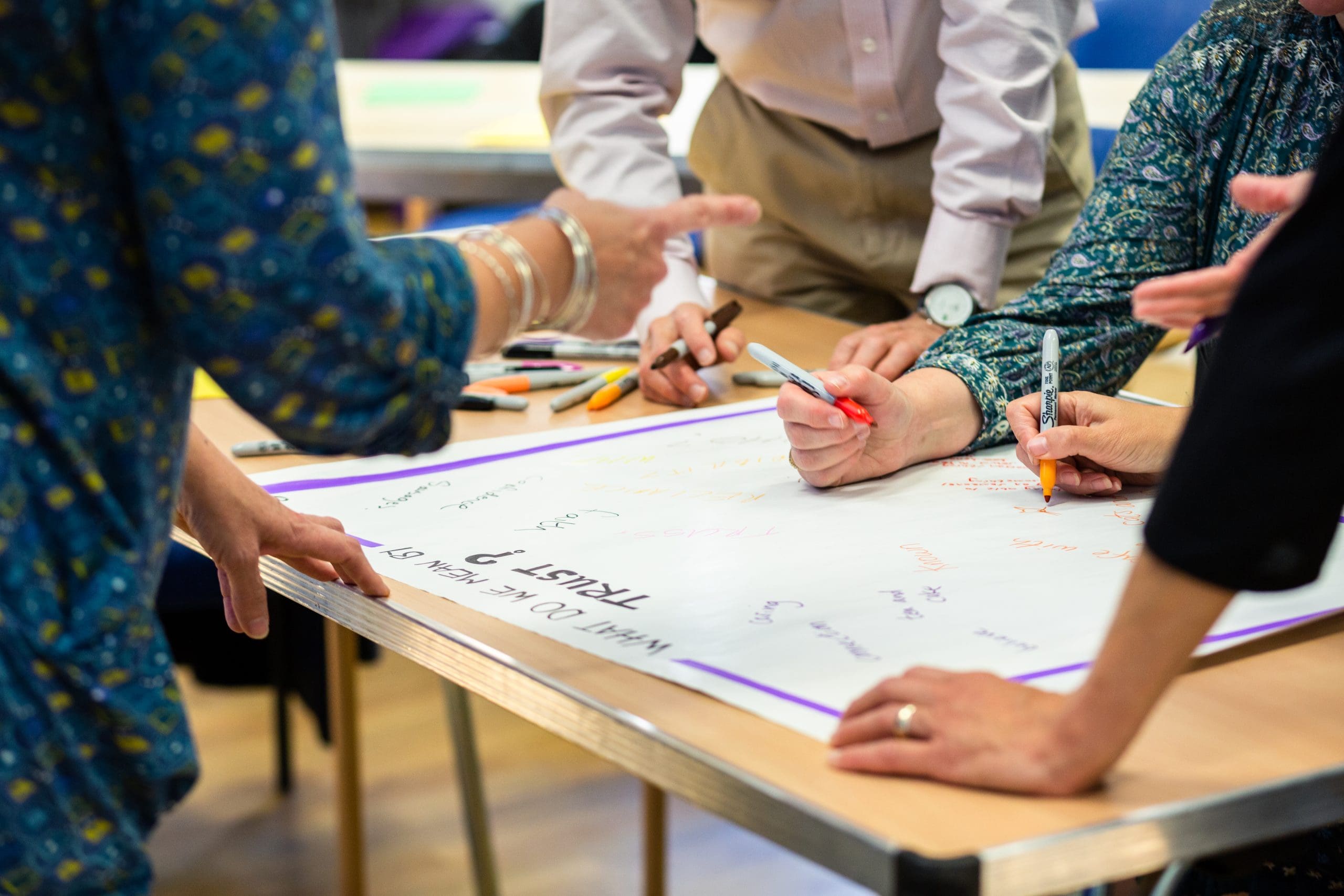 Facilitator leading a workshop with a diverse group of participants seated around the room, engaging in discussion and learning, smiling