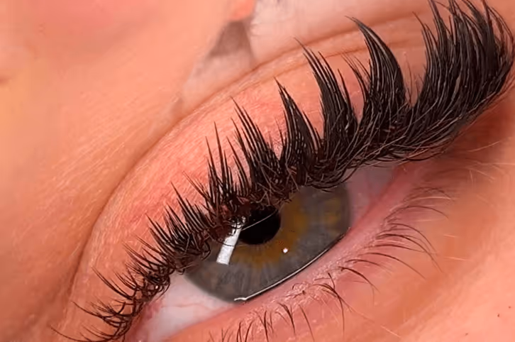 Close-up of an eye with long, dark, curled eyelashes and a greenish-brown iris.