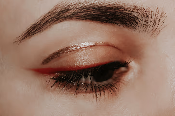 Close-up of a closed eye with bold red eyeliner, shimmering gold eyeshadow, and thick eyelashes.