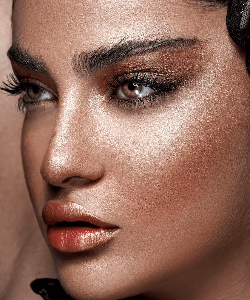Close-up of a woman's face with flawless makeup, highlighting brown eyes, long eyelashes, and glossy lips.