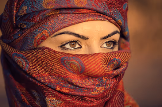 Close-up of a woman with brown eyes wearing a red patterned headscarf covering her hair and lower face.