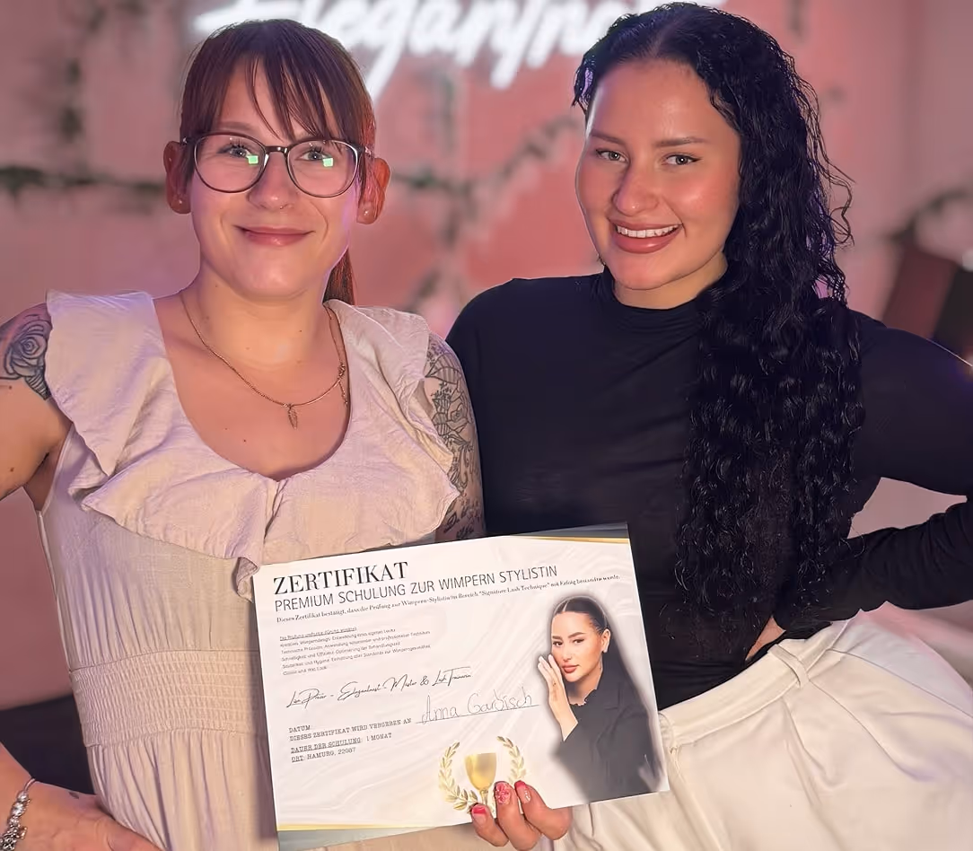 Lisa with student holding a certificate for premium eyelash stylist training, one wearing glasses and the other with long curly hair.