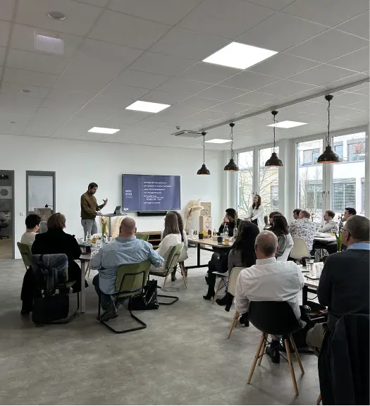 Person hält eine Präsentation vor einer Gruppe von Menschen in einem modernen, hellen Konferenzraum mit großen Fenstern.