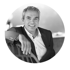 Lächelnder älterer Mann in einem Anzug, der sich entspannt auf einer Bank zurücklehnt.