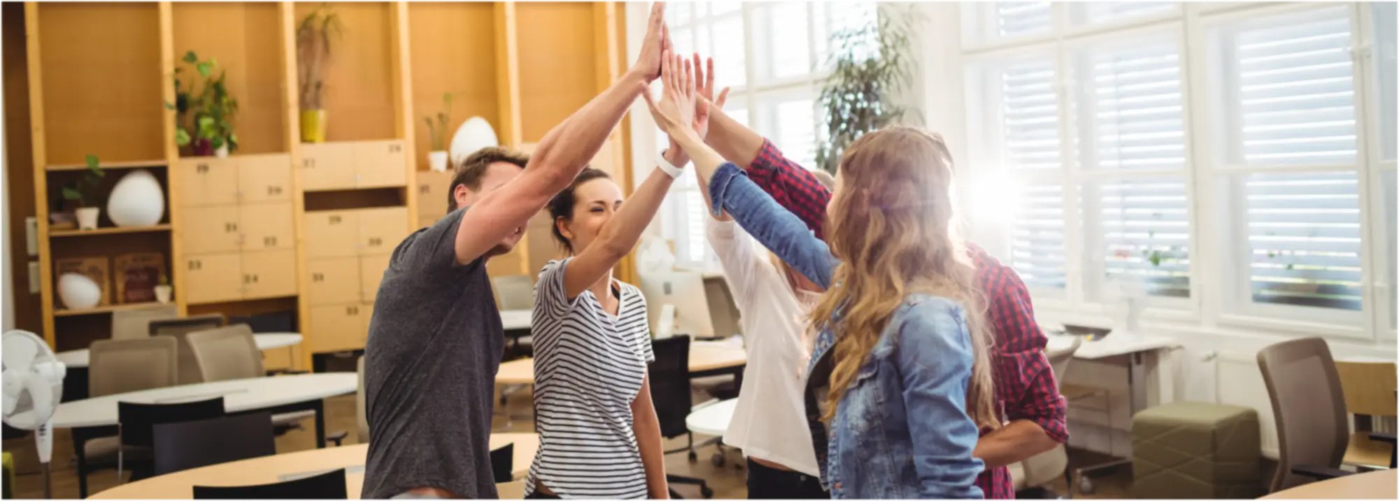 Vier junge Erwachsene in einem hellen Büro geben sich einen gemeinsamen Highfive.