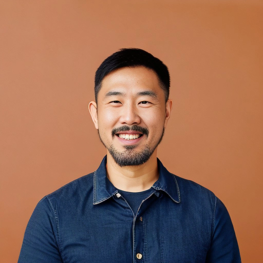 Smiling man with short black hair and beard wearing a dark blue shirt against a brown background.