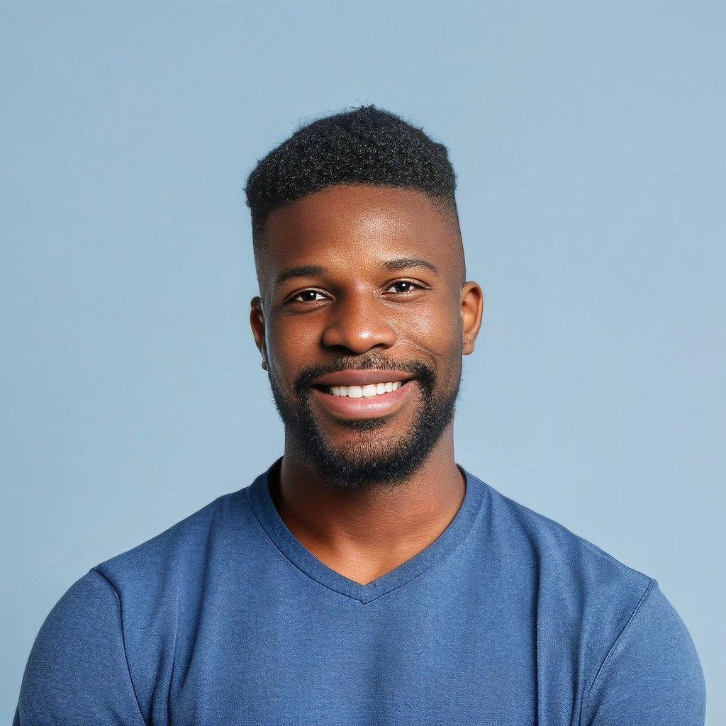 Smiling young Black man with short curly hair and a beard wearing a blue V-neck shirt against a light blue background.