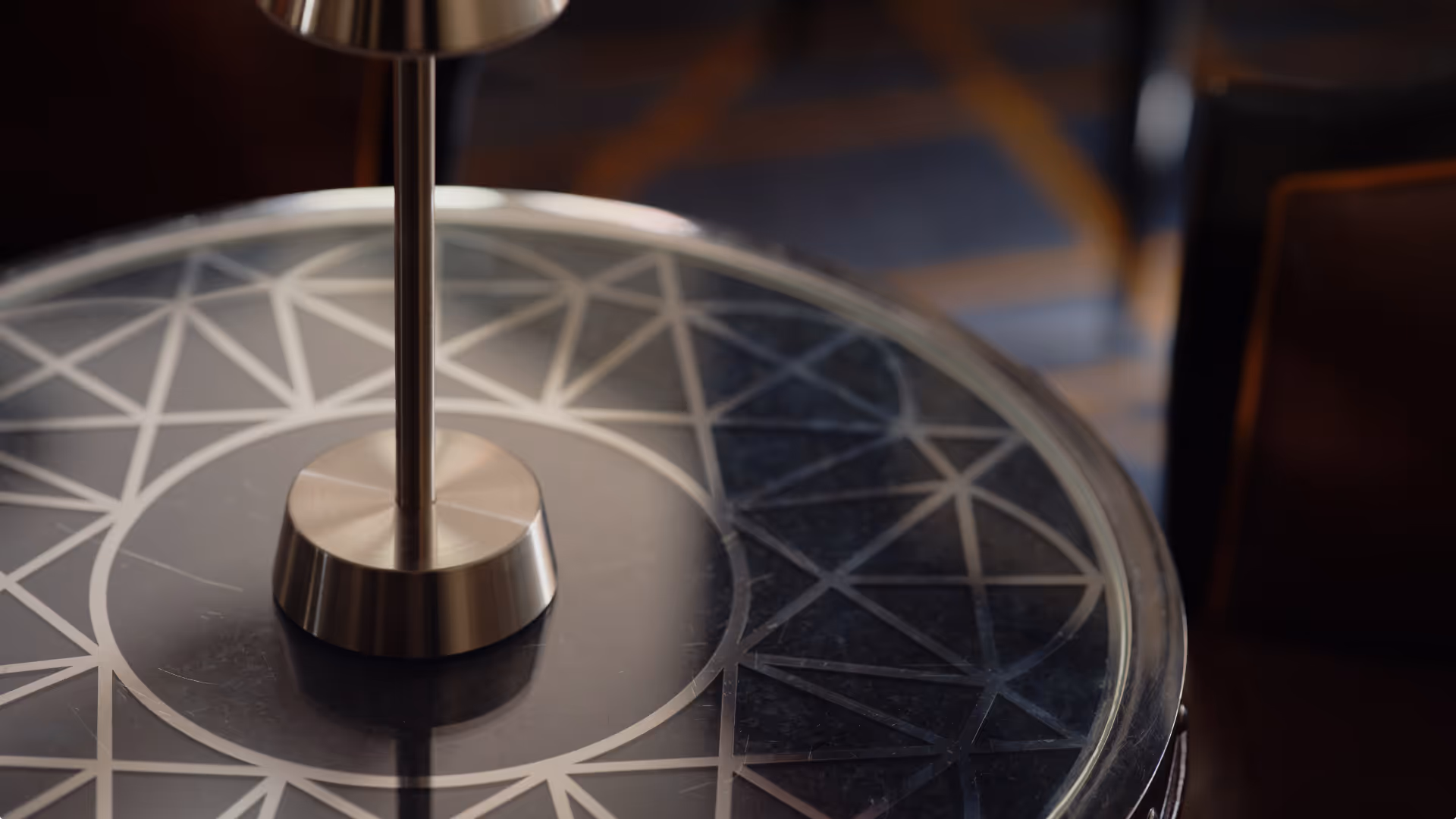 Close-up of a decorative glass tabletop with geometric patterns and a metal lamp base in the center.