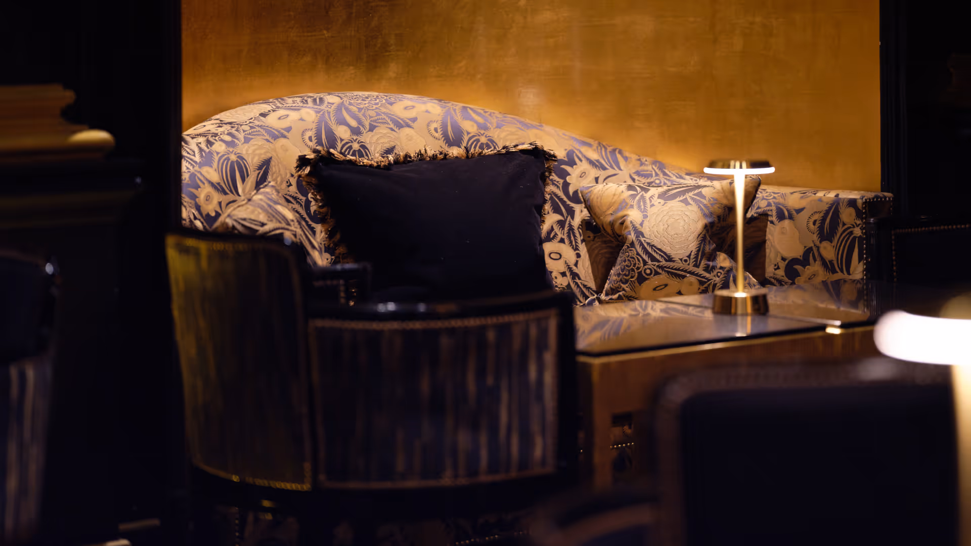 Cozy seating area with patterned sofa, decorative pillows, and a modern table lamp on a reflective coffee table.