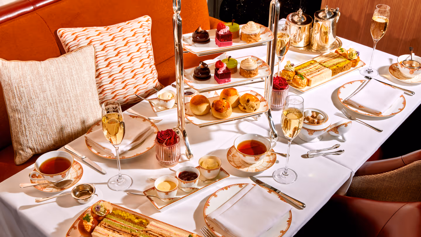 Elegant afternoon tea setup with tiered trays holding assorted pastries and scones, cups of tea, champagne glasses, and finger sandwiches on a white tablecloth.