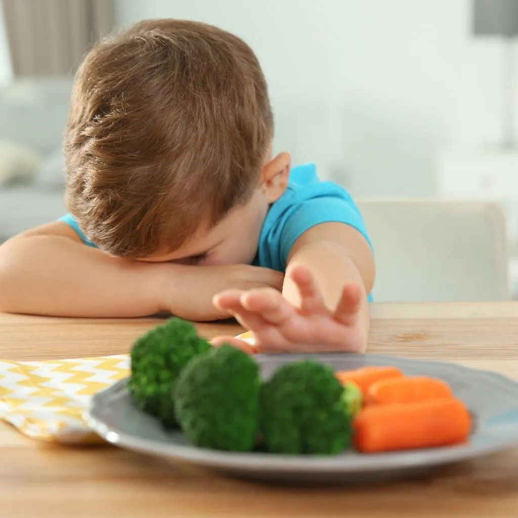 Toddler at dinner table refusing vegetables, illustrating picky eating challenges