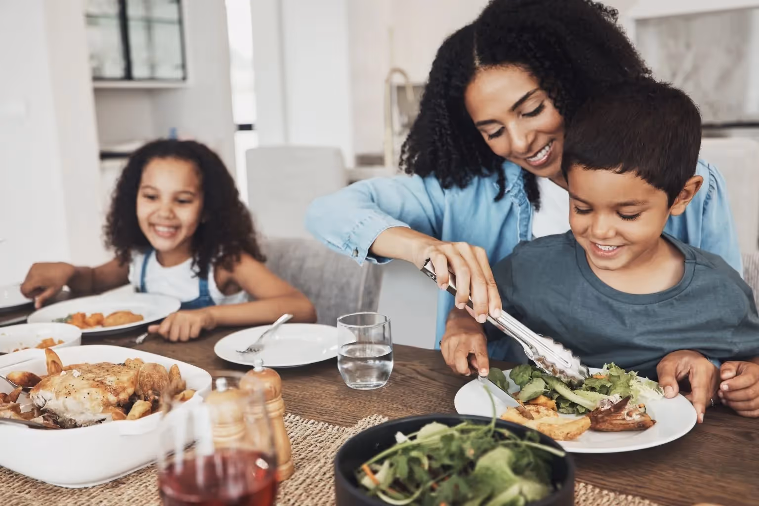 Smiling mother serving healthy food onto her son's plate at a family meal, creating a positive and enjoyable dining experience for children.