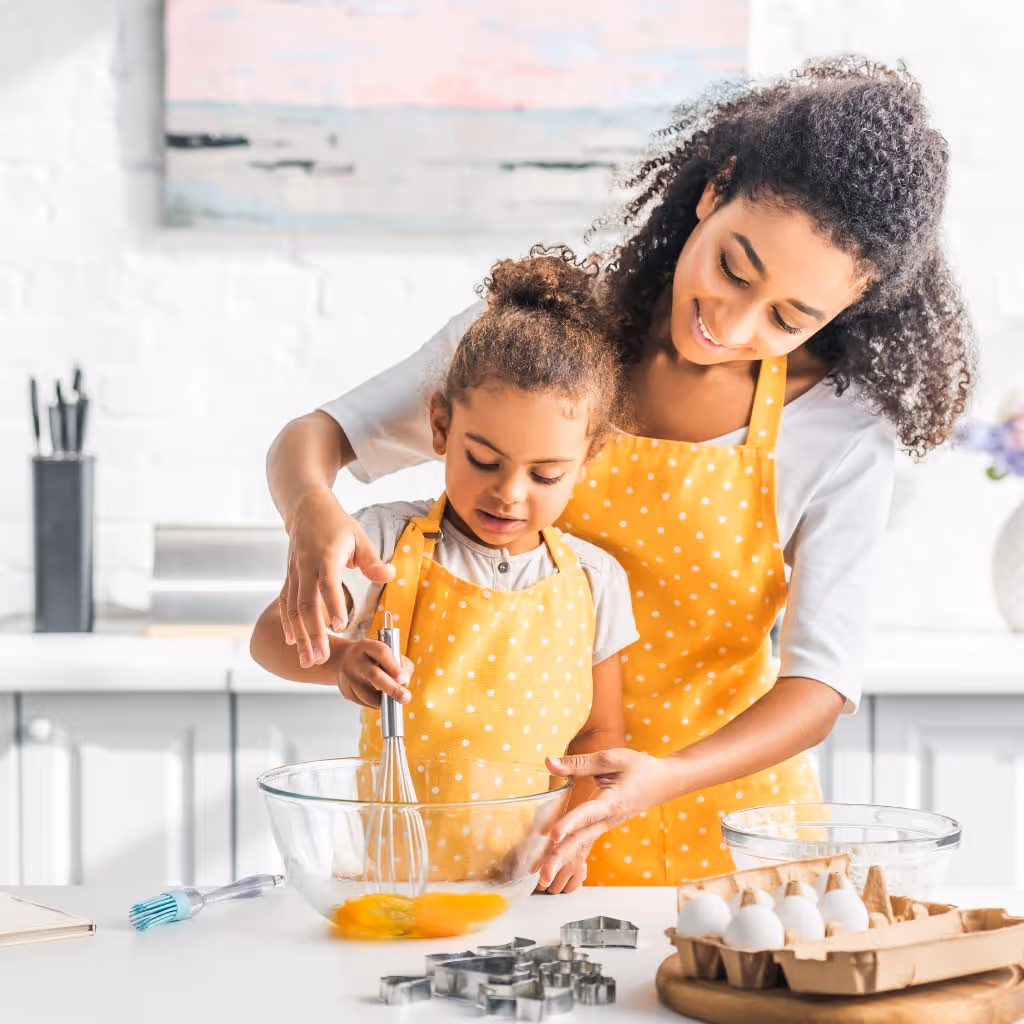 smiling mother helping daughter mixing eggs for dough in kitchen