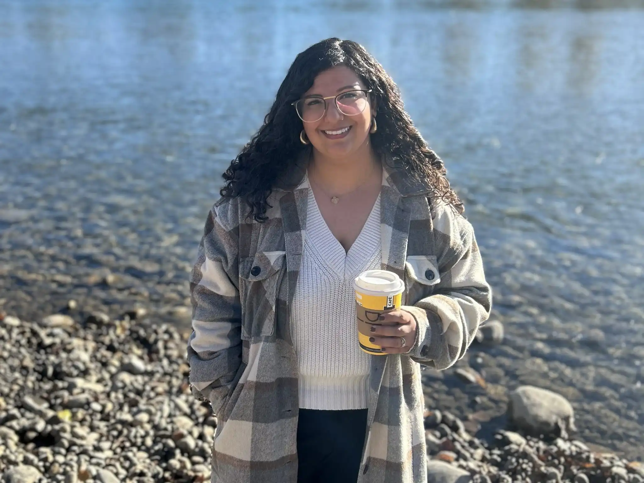 Pooja holding coffee standing near a peaceful river