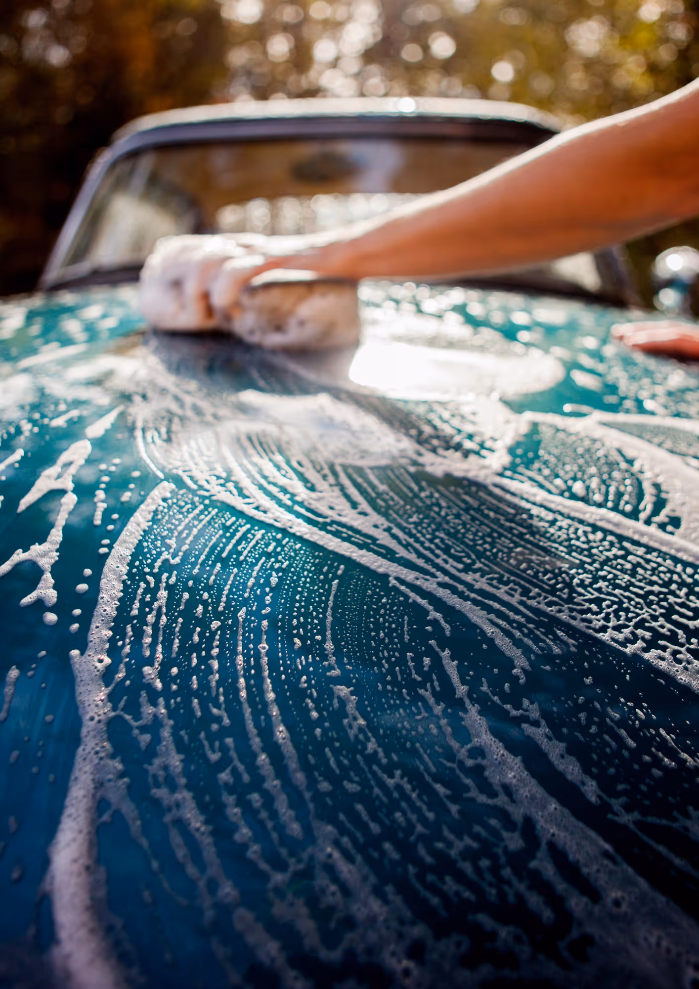 Nahaufnahme einer Hand, die mit einem Schwamm einen schaumigen blauen Autolack reinigt.