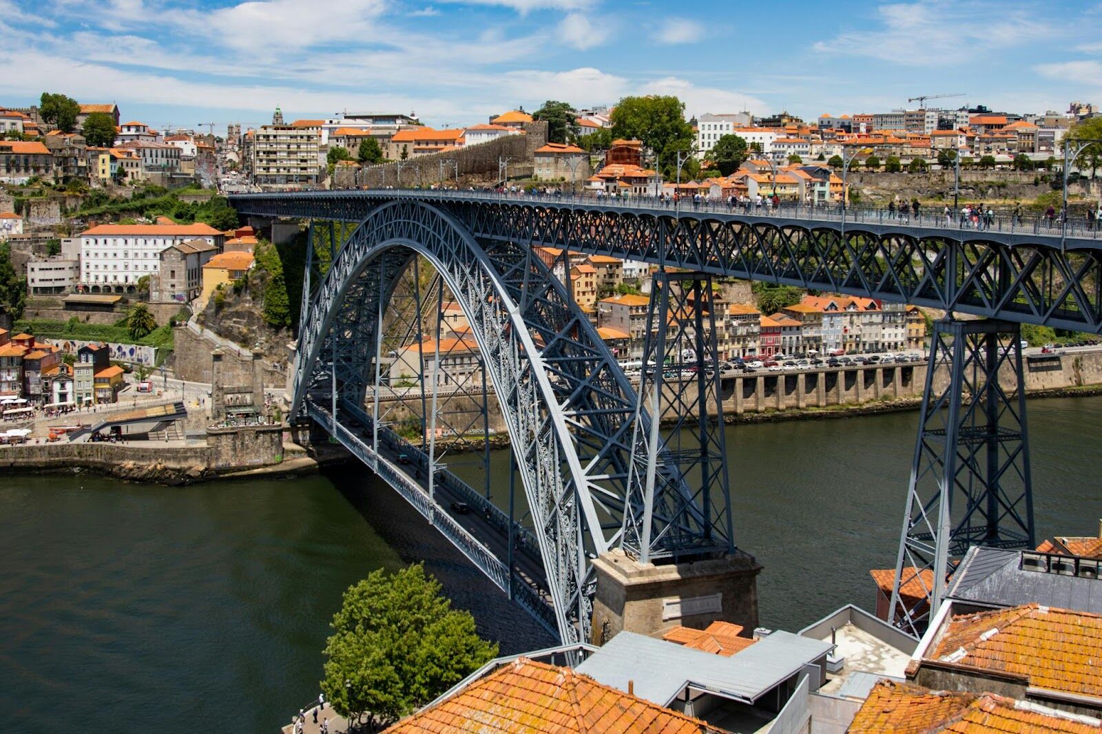 Large iron bridge spanning a river in a vibrant European cityscape.