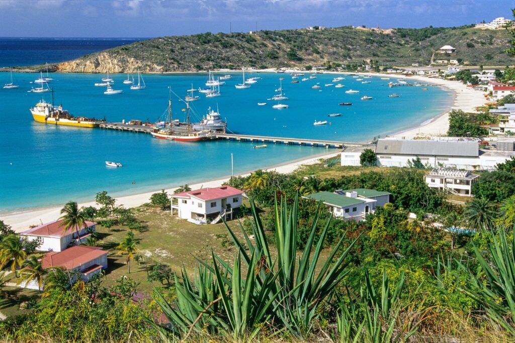 Scenic bay with turquoise water, boats, and colorful houses along the coast of Anguilla.