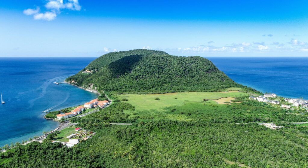 Lush green mountain surrounded by the Caribbean Sea with coastal buildings in Dominica.