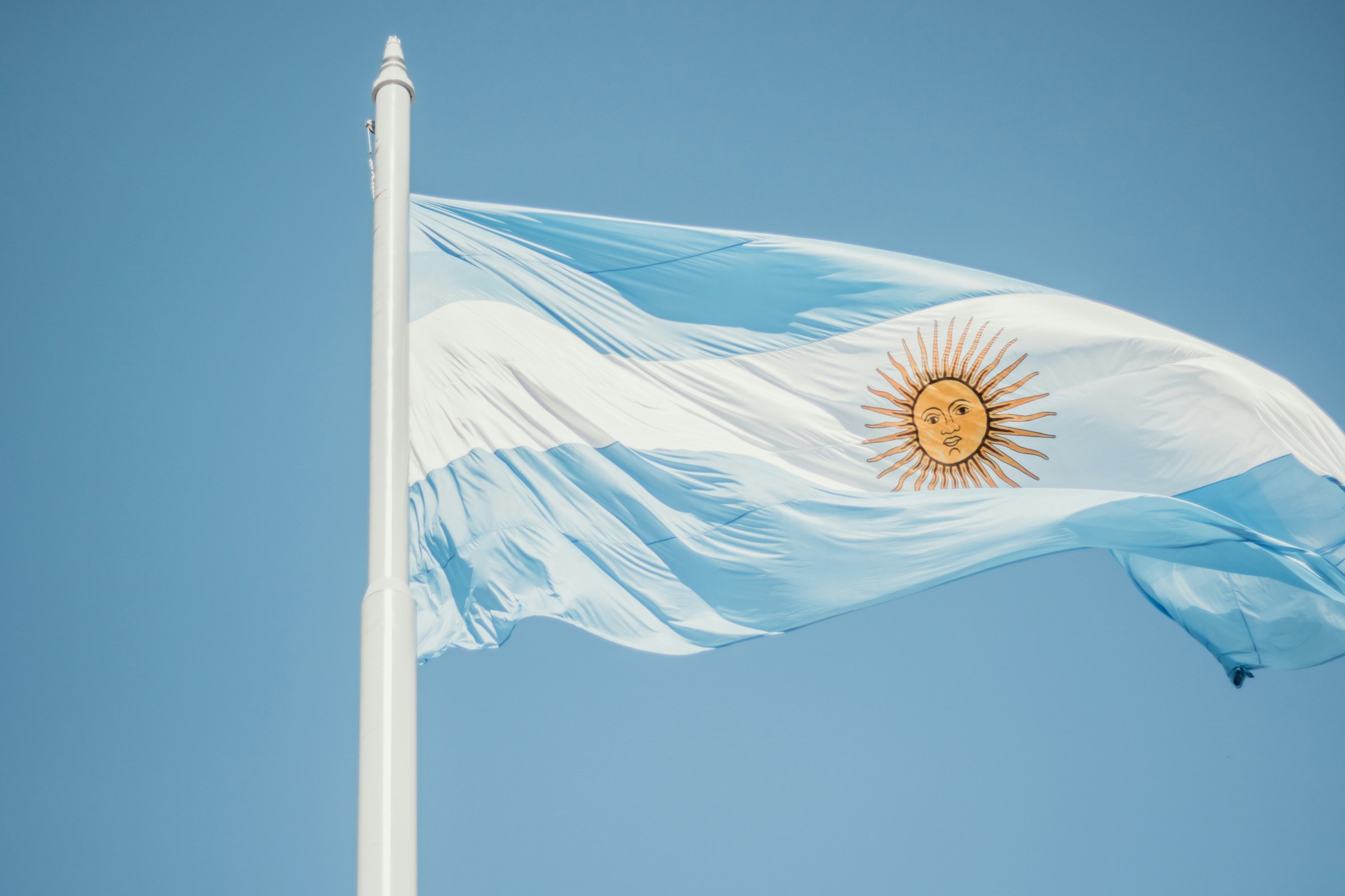 The light blue and white Argentine flag with the golden Sun of May, waving against a clear sky
