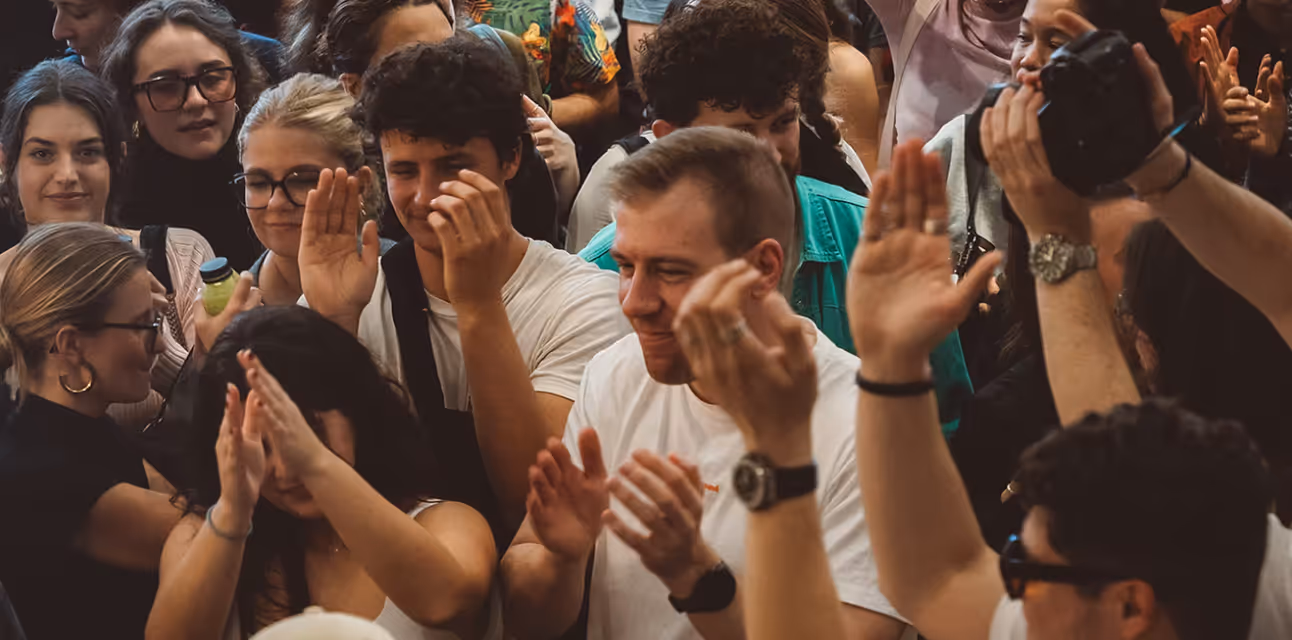 A diverse group of people clapping and smiling closely together in a lively crowd.