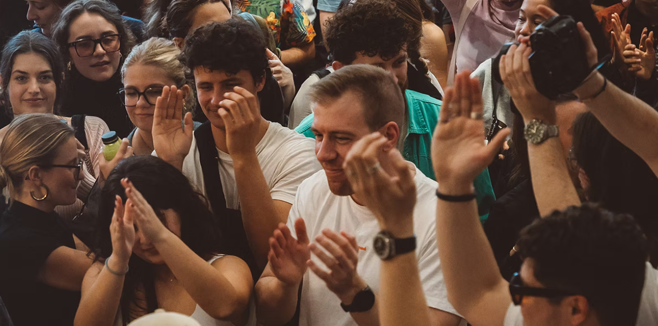 A diverse group of people clapping and smiling closely together in a lively crowd.