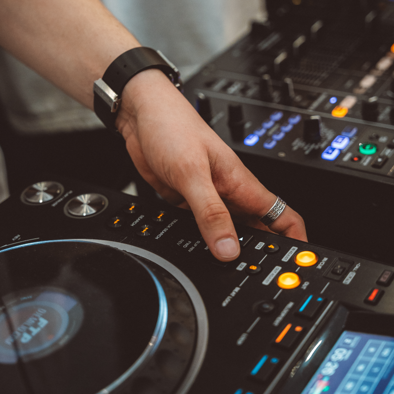 Close-up of a hand adjusting controls on a DJ mixer and turntable with illuminated buttons and knobs.