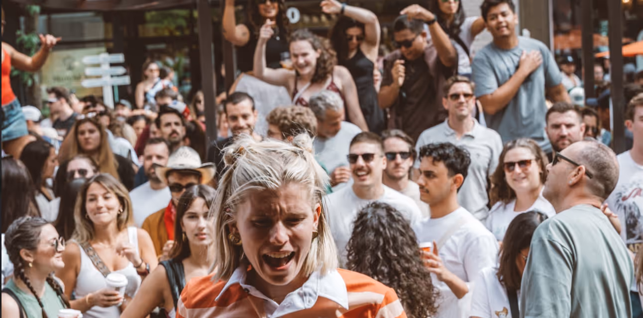 Crowd of people enjoying an outdoor event with a woman in an orange striped shirt laughing in the foreground.