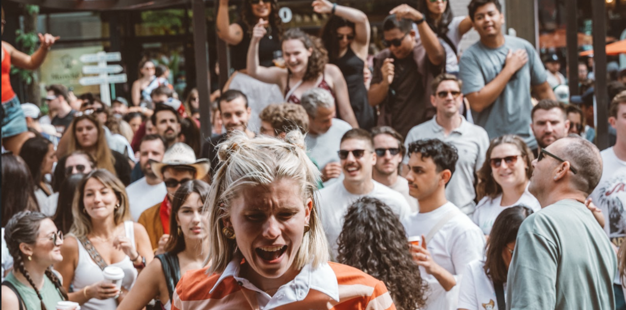 Crowd of people enjoying an outdoor event with a woman in an orange striped shirt laughing in the foreground.