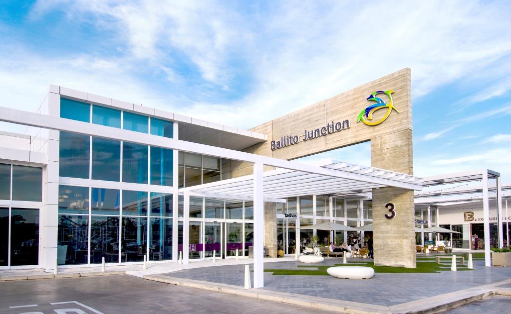 Exterior view of Ballito Junction shopping center with a modern glass and stone facade under a blue sky.
