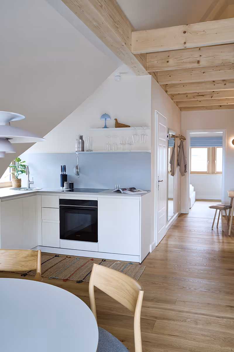 Bright modern kitchen with white cabinets, light wood ceiling beams, and a small window above the sink.