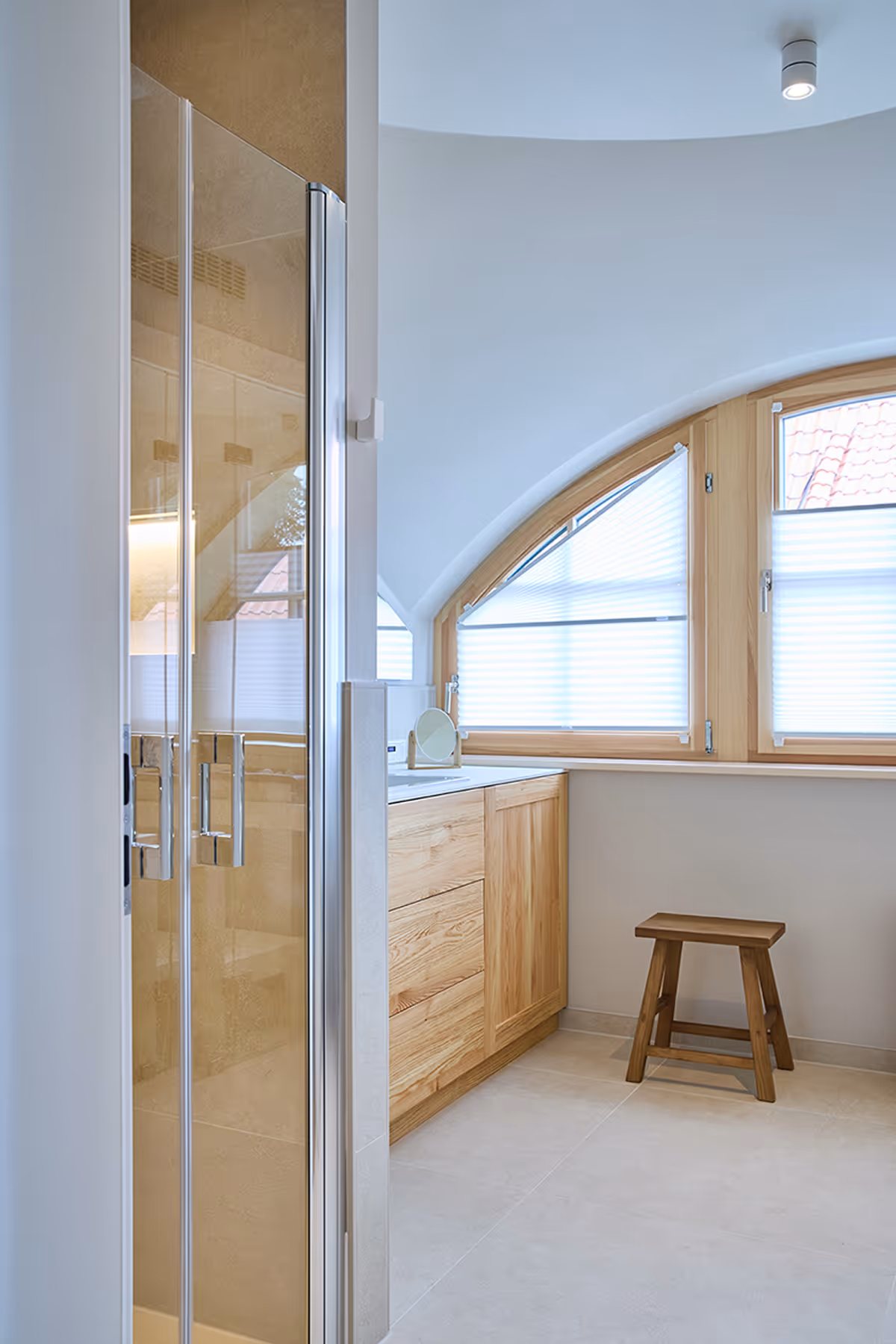 Bright bathroom corner with wooden cabinet, small wooden stool, and curved windows with blinds.