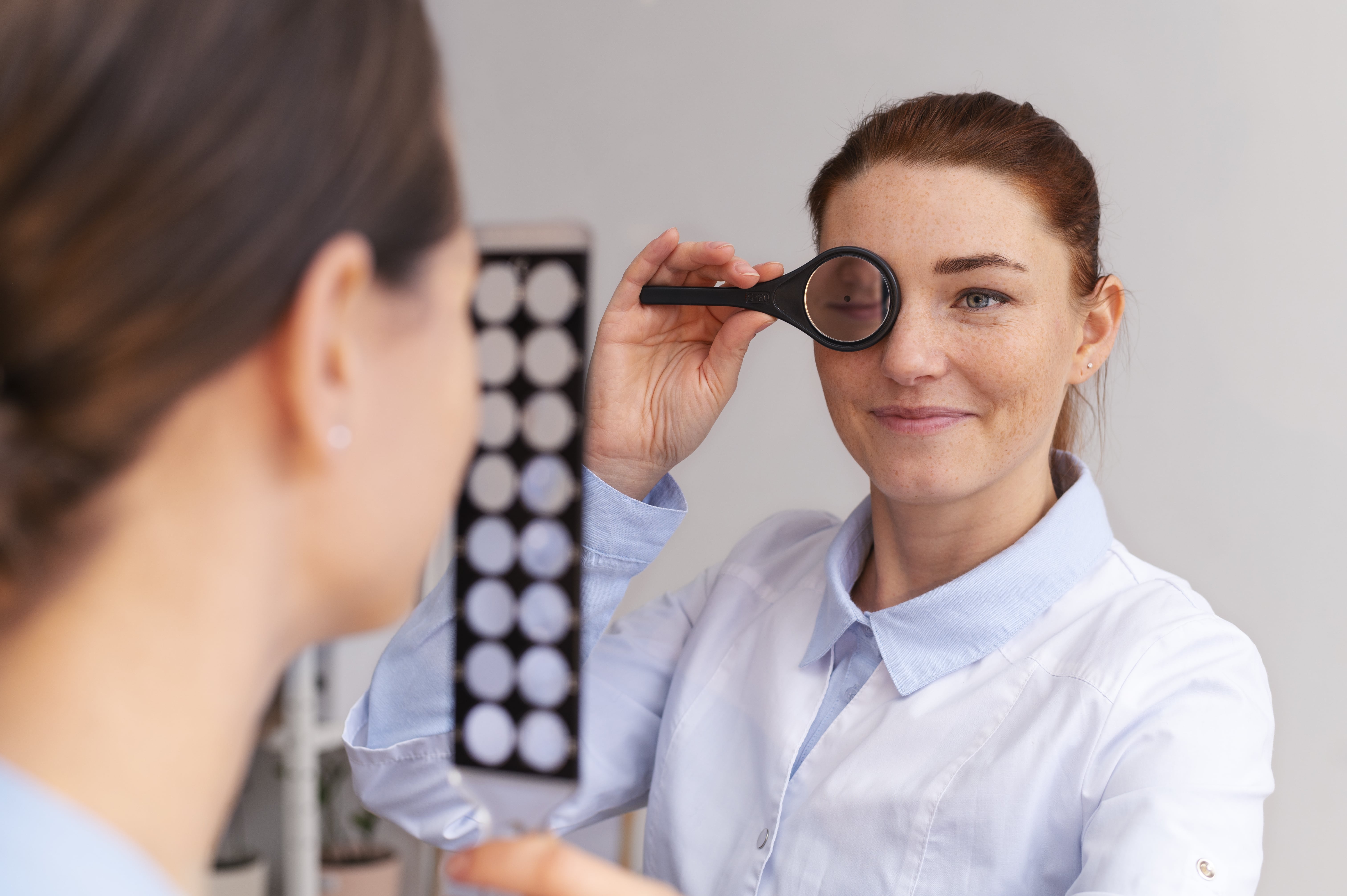 Optometrist examines patient's eye vision using handheld lens during eye exam