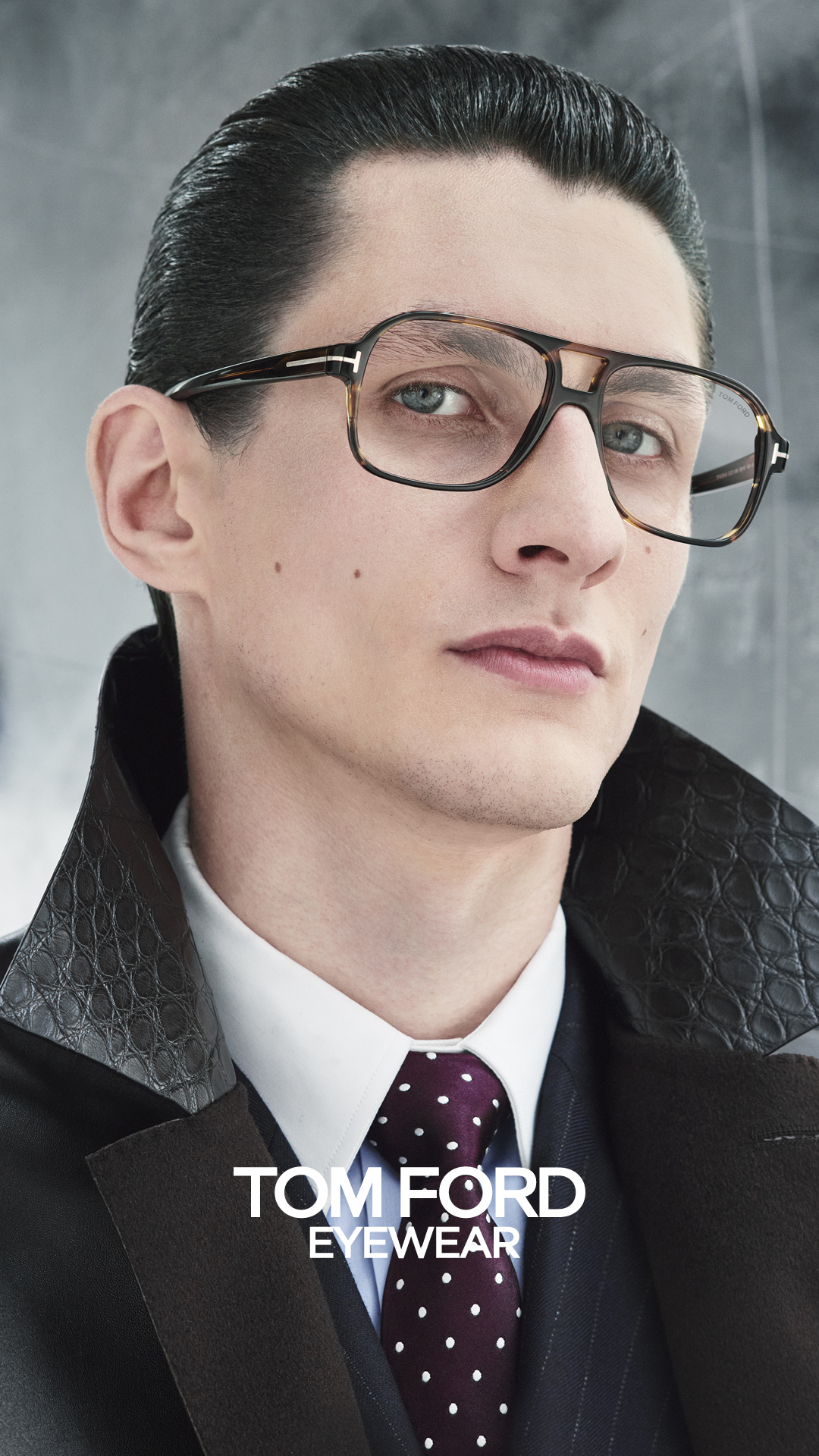 Man wearing Tom Ford tortoiseshell glasses, dark suit and polka dot tie portrait