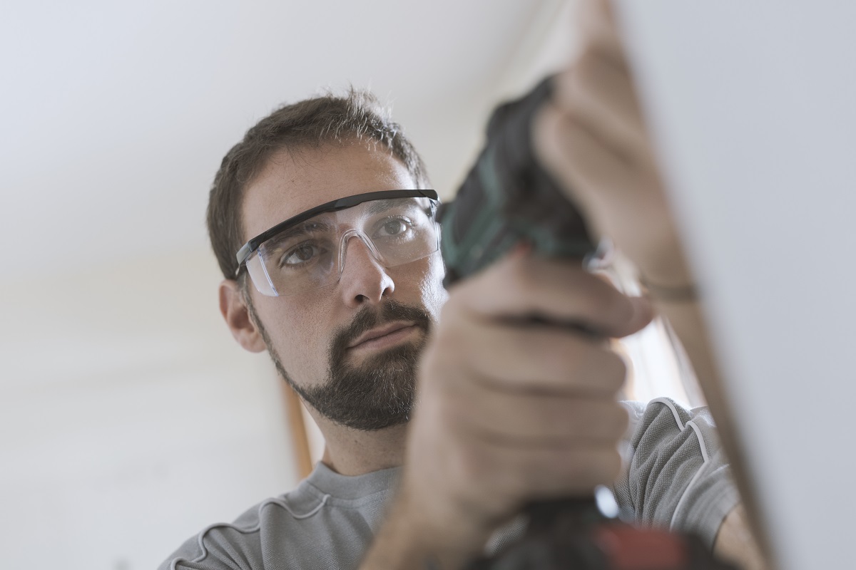 Man wearing safety glasses and gloves examining or working on something out of focus