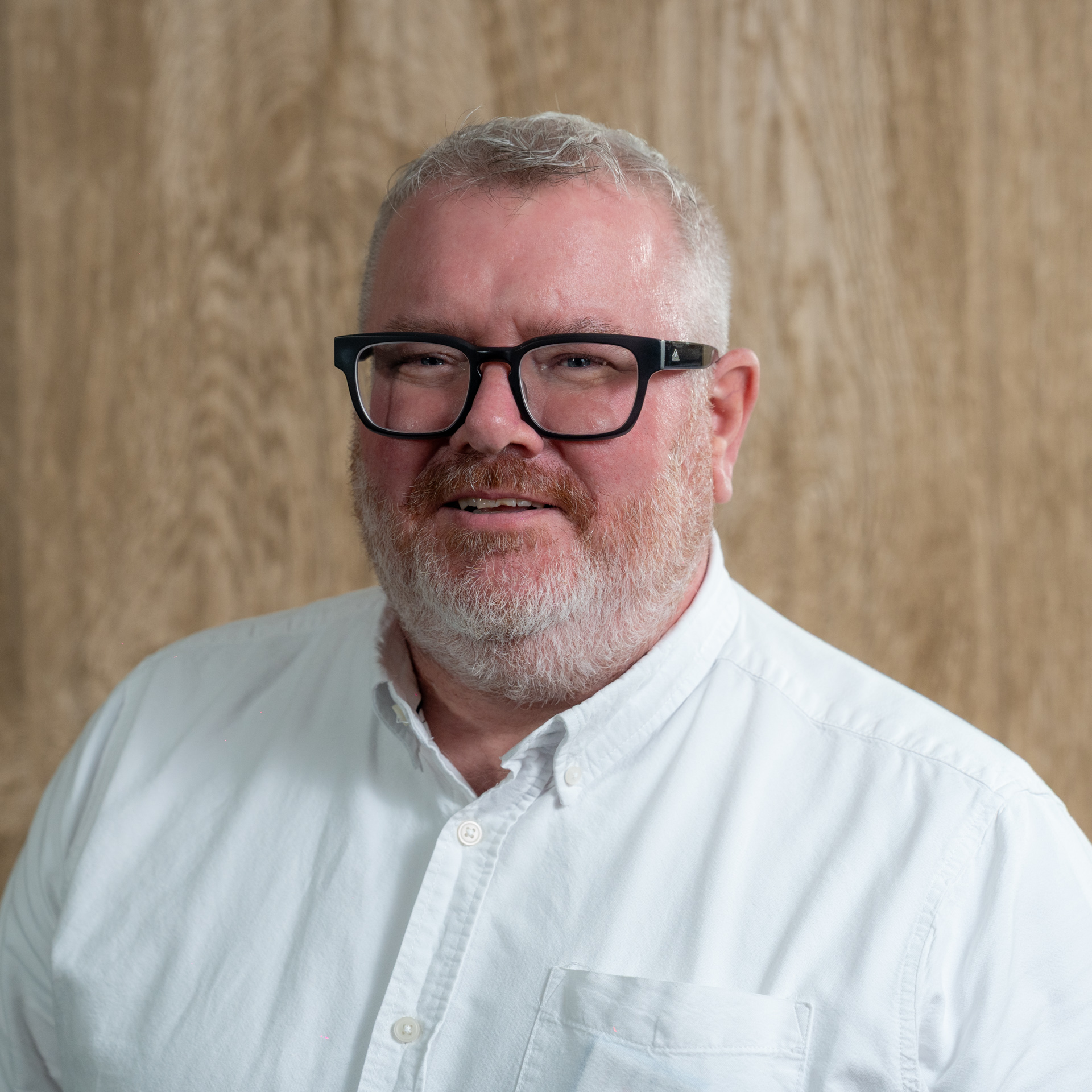 Middle-aged man with gray hair, beard, and black-framed glasses wearing white button-up shirt