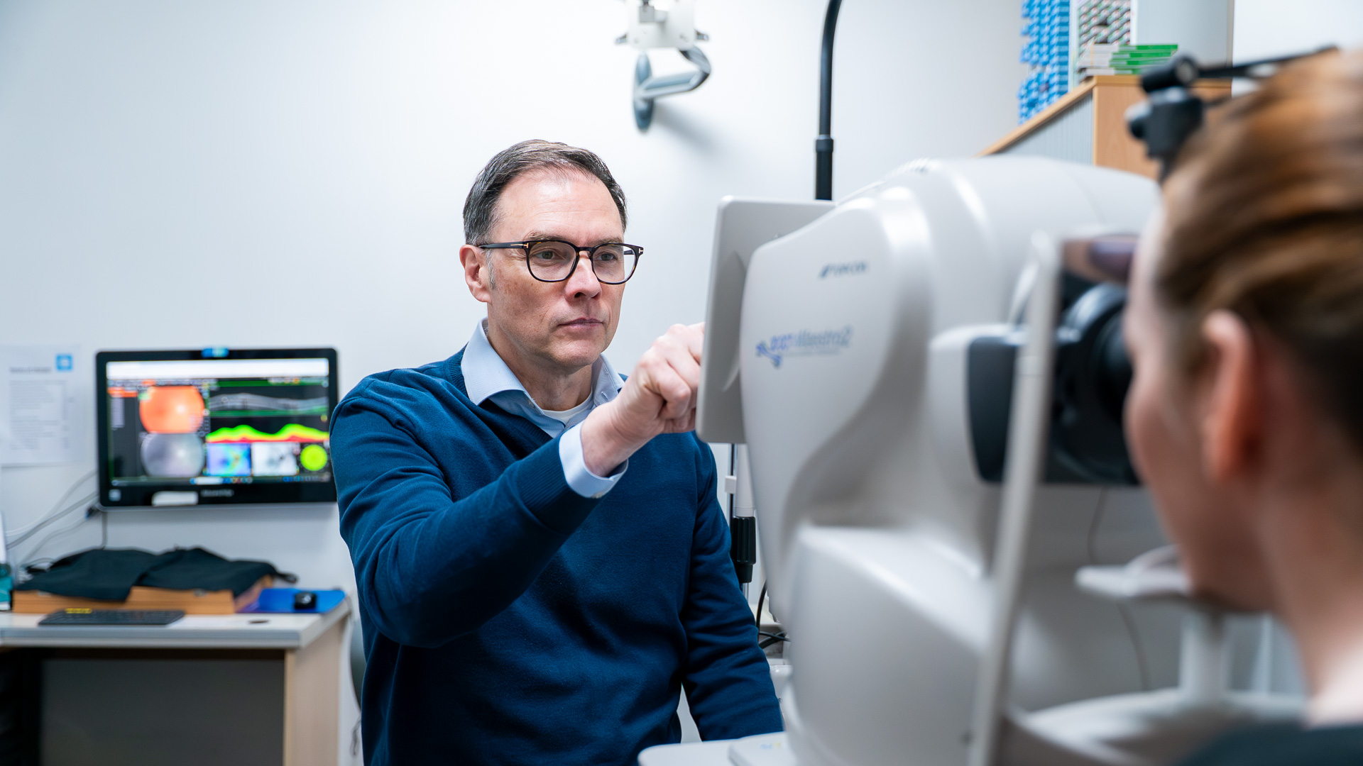 Man in blue shirt operates medical imaging equipment in laboratory with computer monitors.