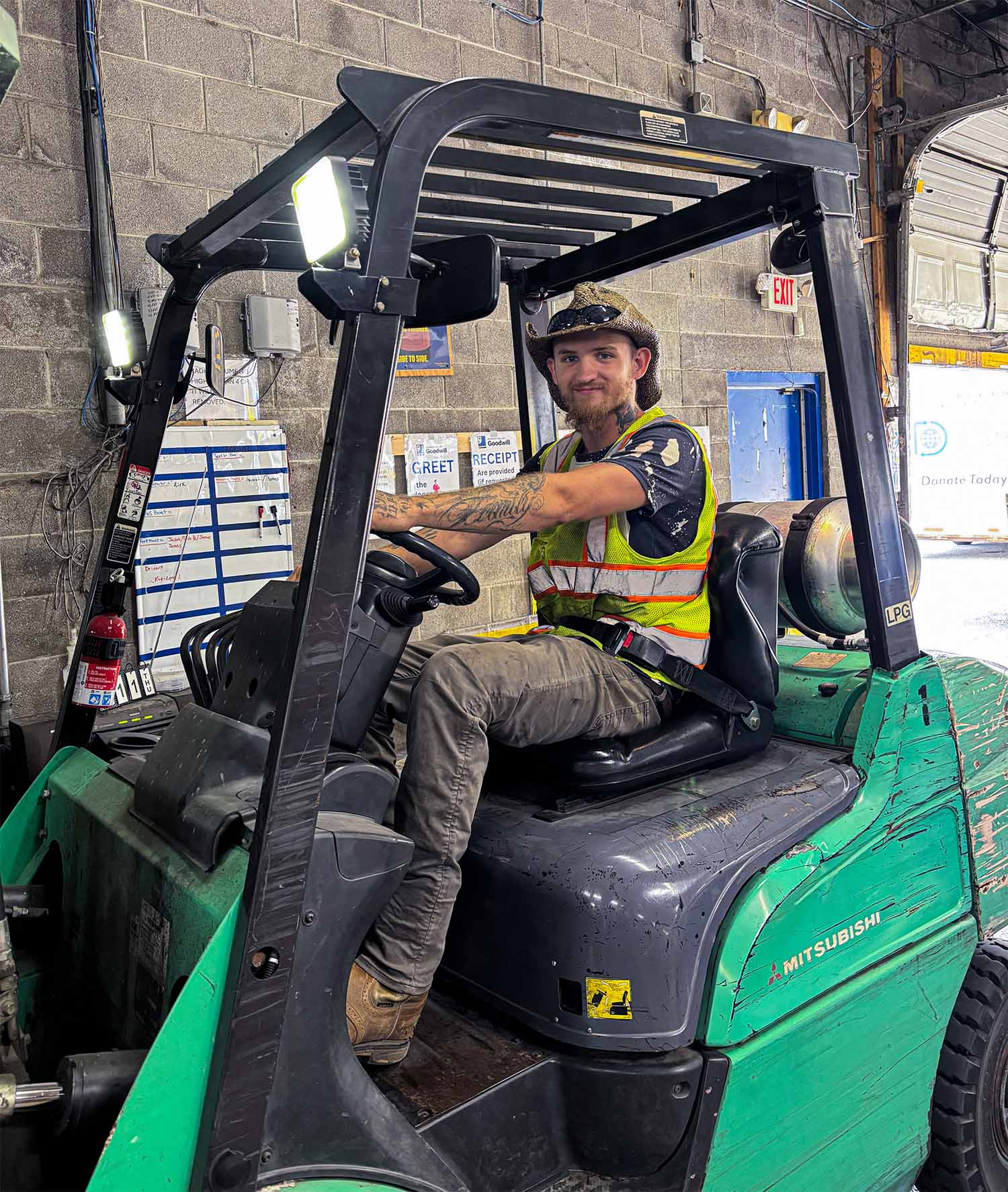 A Goodwill team member wearing a reflective safety vest sitting on a Mitsubishi forklift in a warehouse.