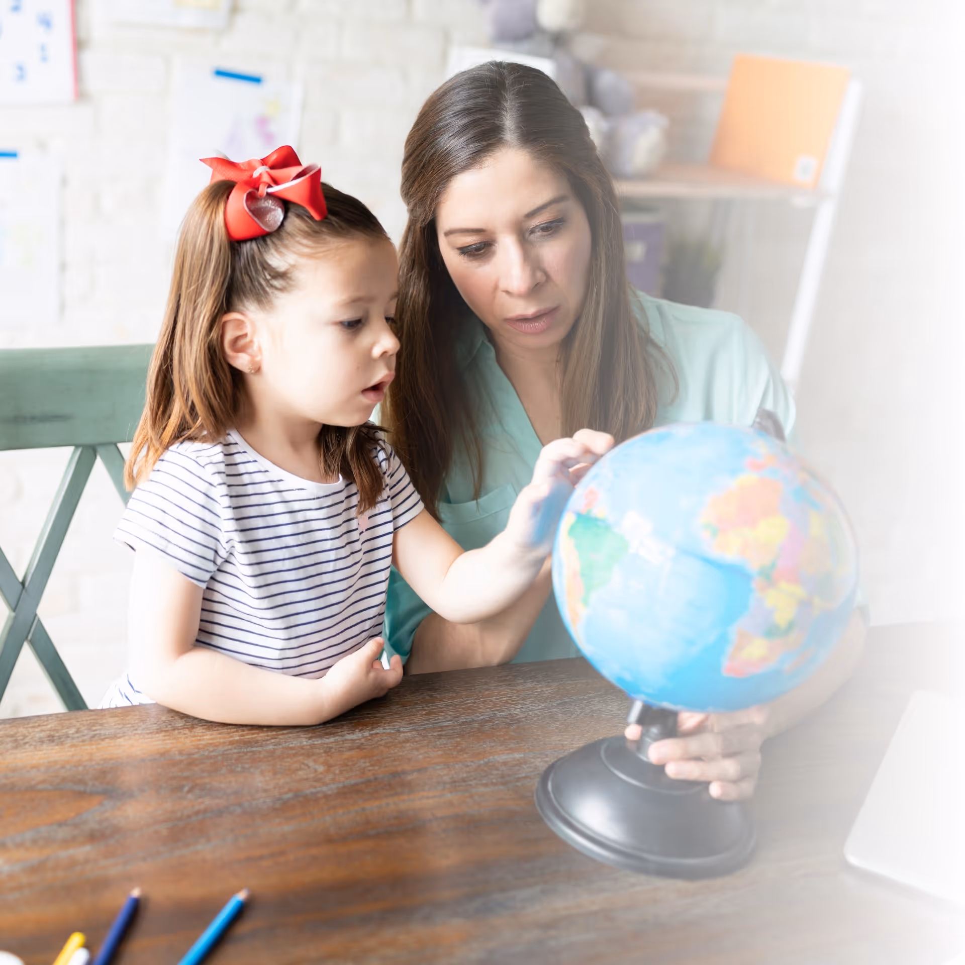 A young girl looking at a world globe on a desk with her mother.