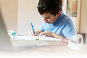 A young male, writing with a blue pen on a piece of paper.