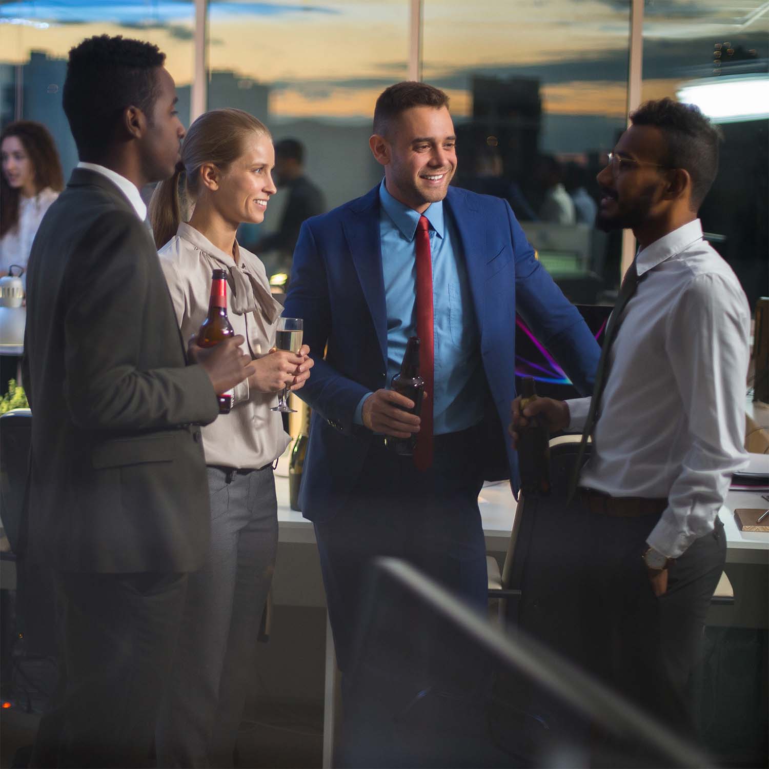 Vier collega's in zakelijke kleding praten en houden drankjes vast tijdens een informeel kantoorfeest bij zonsondergang.