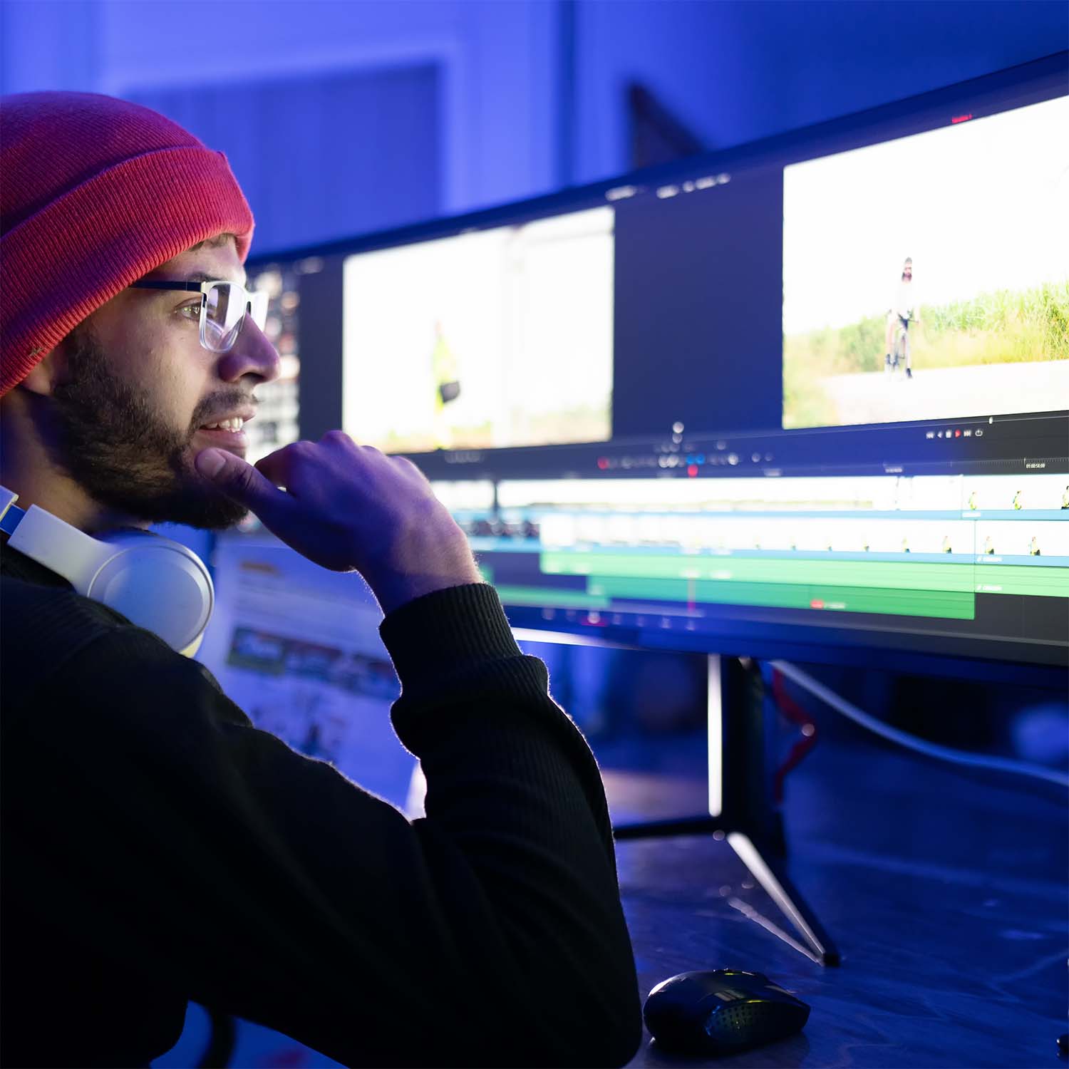 Man met rode muts en bril kijkt naar grote monitor met videobewerkingssoftware.