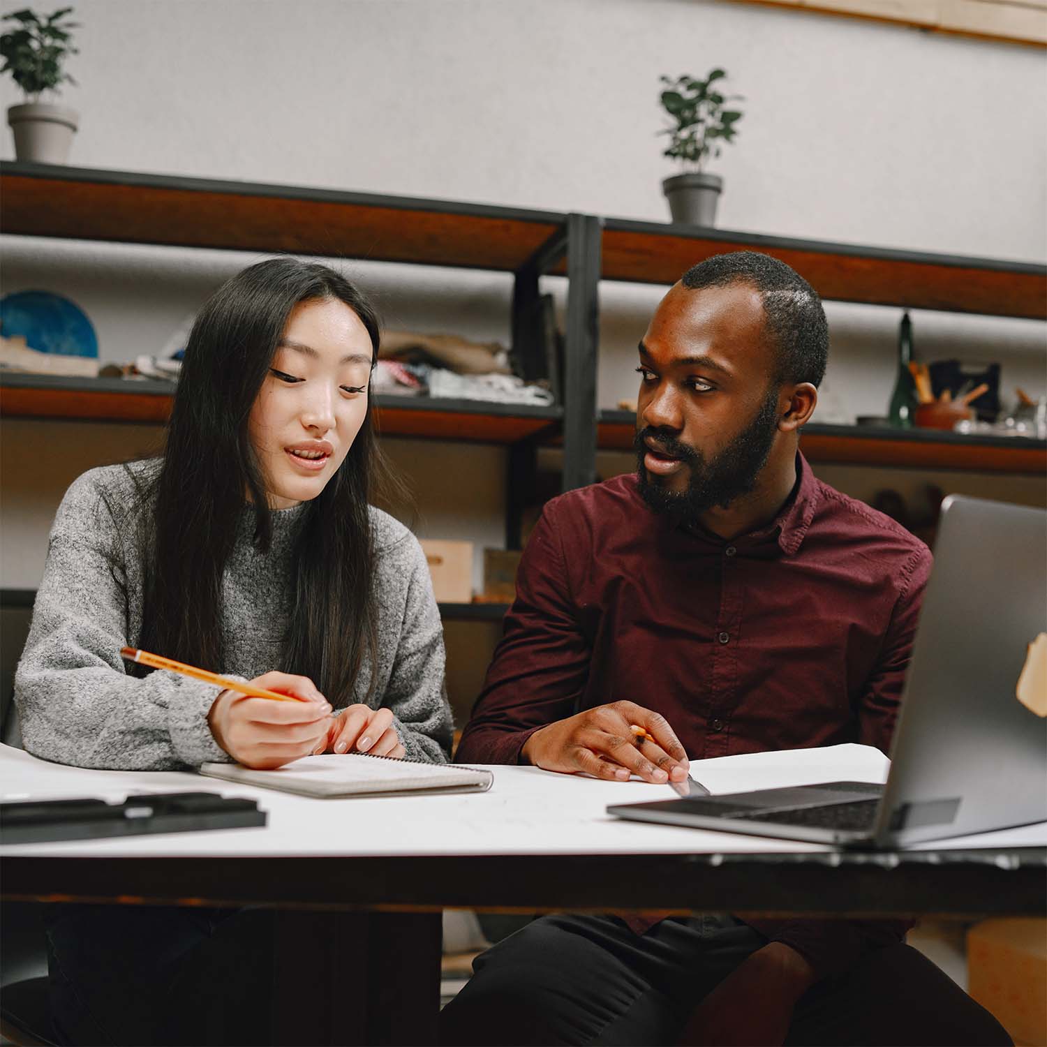 Twee collega's werken samen aan een project met een notitieboek en laptop aan een tafel.