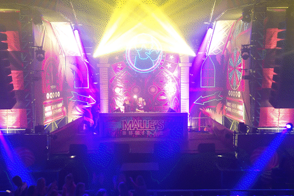 DJ's achter een verlicht podium bij Malle's Bierbar met kleurrijke lichten en een feestelijk publiek.