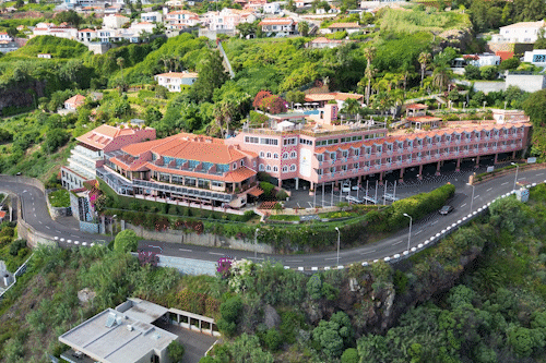 Luchtfoto van een hotel met rode daken op een groene heuvel, omgeven door wegen en huizen.