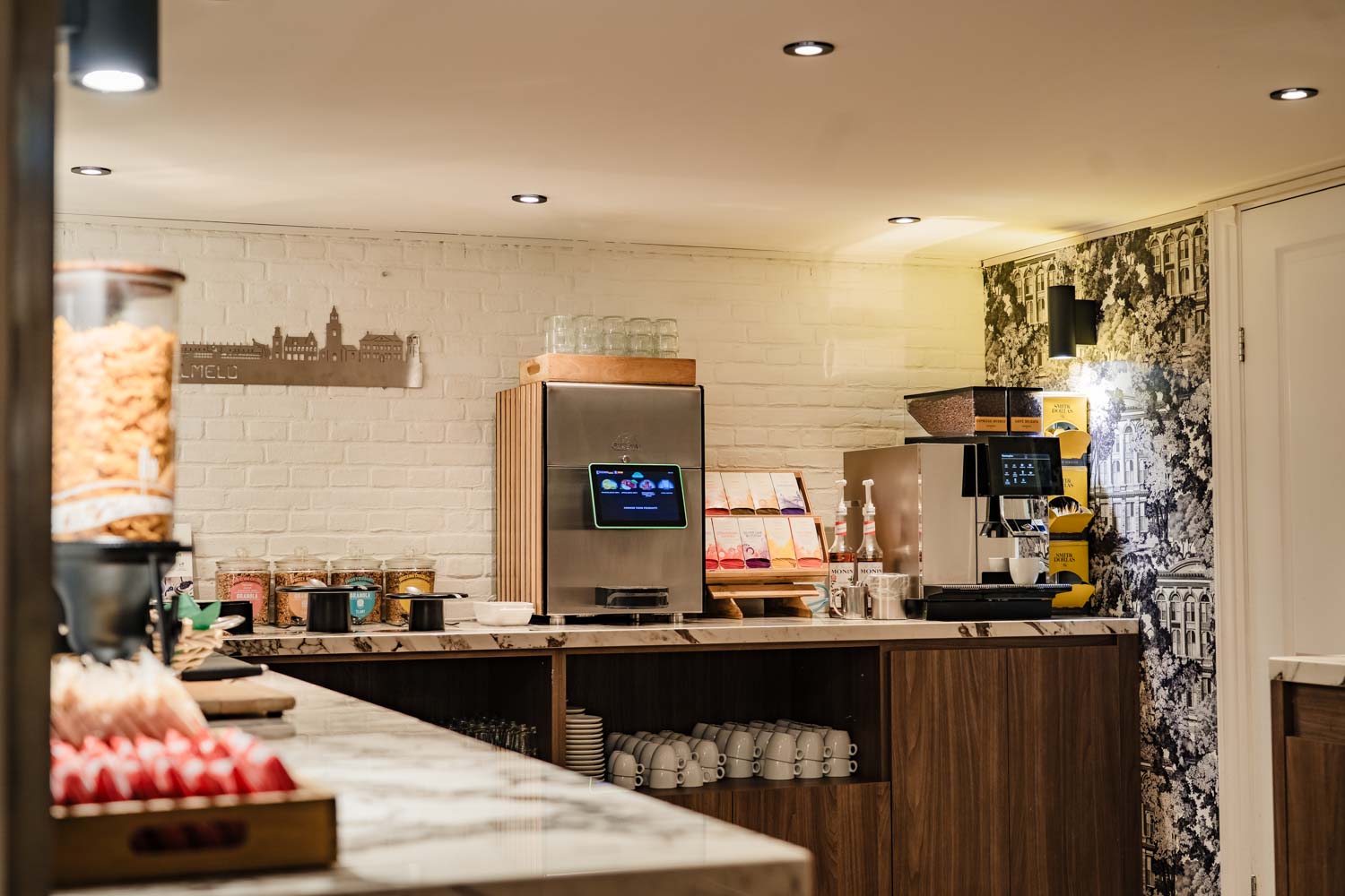 Moderne ontbijtruimte met koffieautomaten, granola en kopjes op een marmeren aanrecht.
