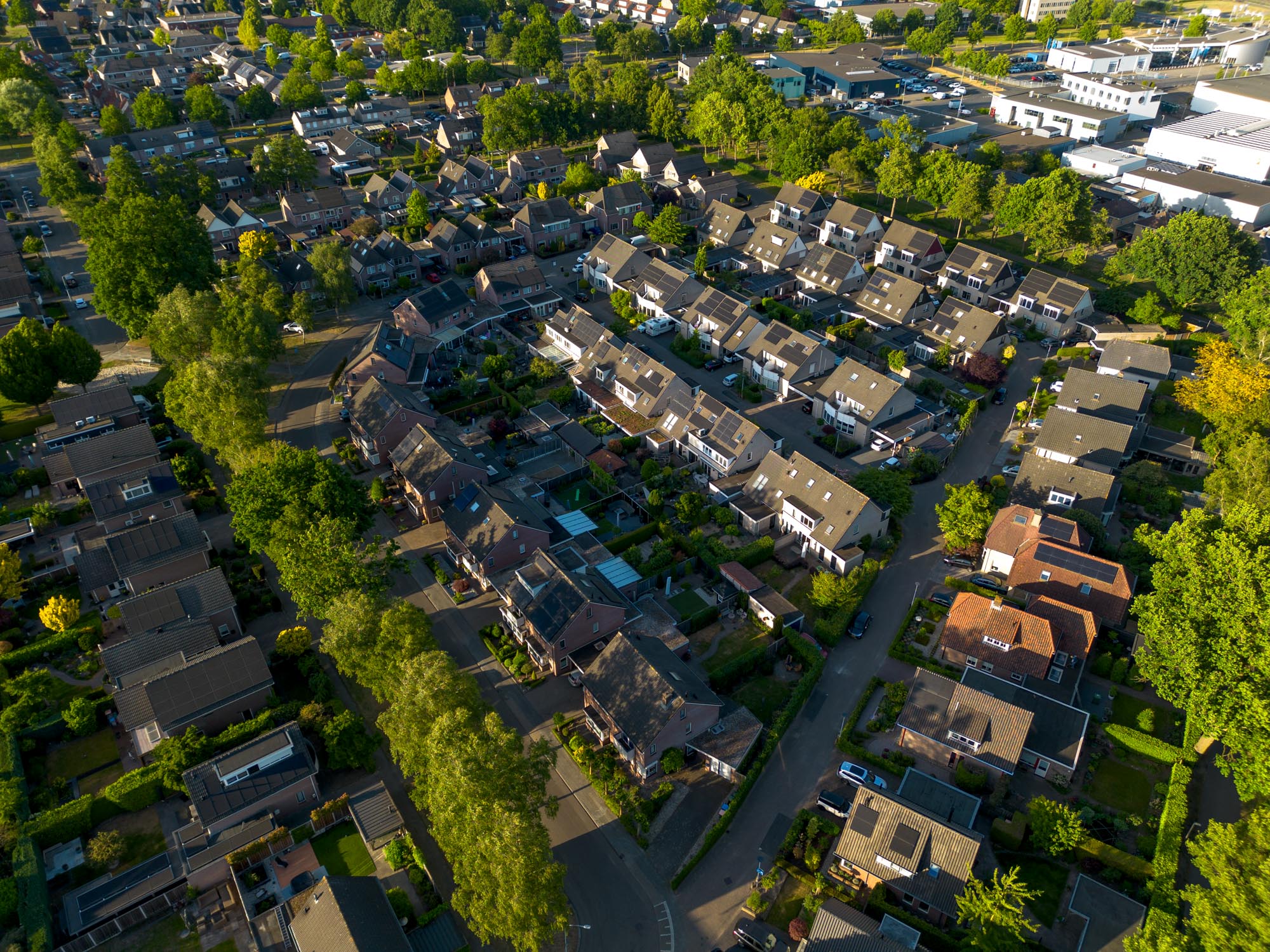 Luchtfoto van een woonwijk met huizen, bomen en straten in zonlicht.