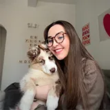 Jeune femme avec des lunettes souriante tenant un chiot blanc et marron à l'intérieur.